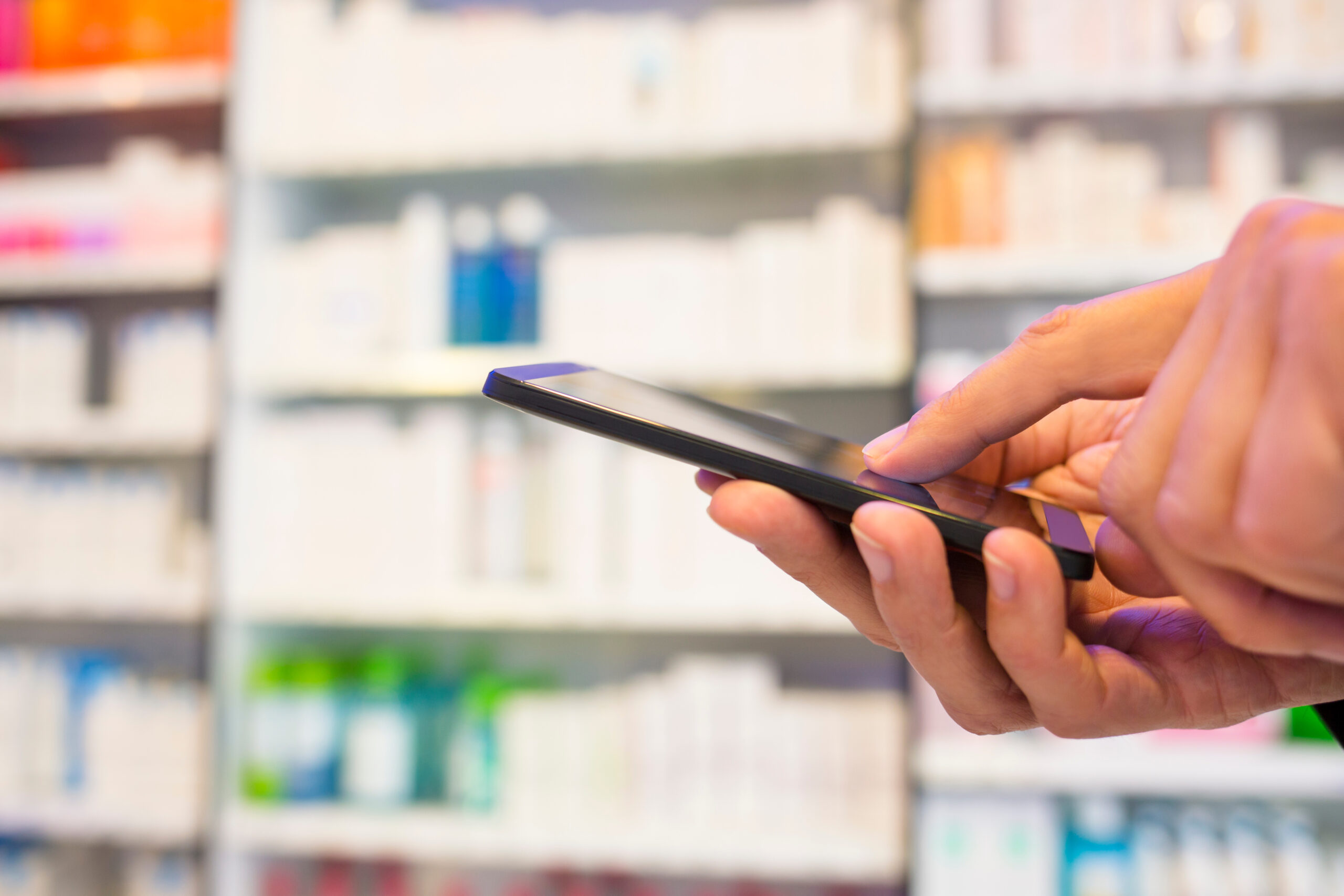 Hand holding mobile phone in pharmacy.